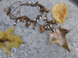 Mässingsplåt, sågad, patinerad och etsad, patinerad kopparkedja, Vintaj koppartråd för öglor, handgjorda pärlnålar i patinerad koppar. Diverse fröpärlor och tigerjaspis-chips.